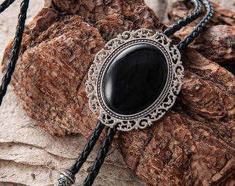 May include: A black oval stone bolo tie with a silver filigree frame. The braided black leather cord has decorative silver tips. The bolo tie is a classic Western accessory.