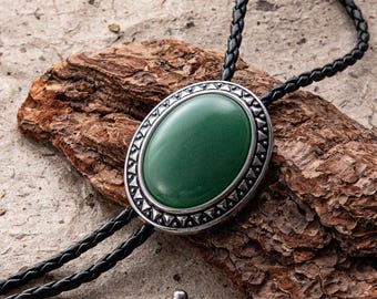 May include: A bolo tie featuring a large, oval, green stone set in a silver-toned frame with a decorative edge. The tie has a braided black leather cord.