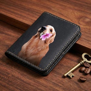 May include: Black leather wallet featuring a golden retriever with a pink flower in its mouth. The wallet has white stitching around the edges. A vintage key and coffee beans are on a wooden surface.