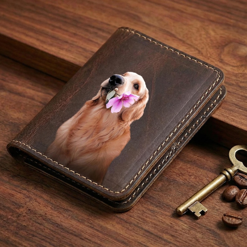 May include: A brown leather wallet featuring a golden retriever holding a pink flower in its mouth. The wallet has a stitched border and a vintage aesthetic. A bronze key and coffee beans are next to the wallet.