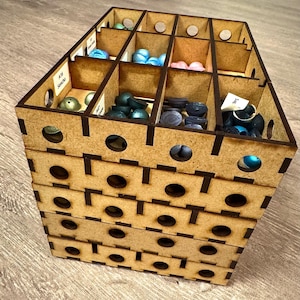 Könnte beinhalten: Ein mehrteiliger Holzorganizer mit verschiedenen bunten Perlen und kleinen Objekten. Der Organizer besteht aus hellbraunem Holz und hat eine Reihe rechteckiger Fächer. Die Fächer sind mit blauen, grünen, rosa und schwarzen Perlen gefüllt. Der Organizer hat ein Etikett mit der Aufschrift "A16 Sencha".