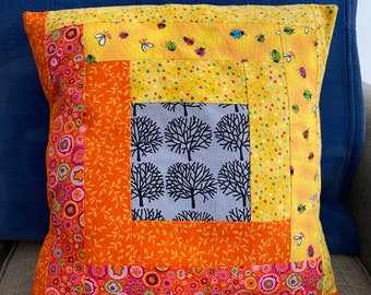 Peut inclure: Un coussin de patchwork jaune, orange et gris avec un motif d'arbres au centre. Le coussin a une bordure en tissu orange à motif de feuilles et une bordure en tissu rose et orange à motif de cercles.