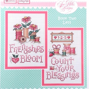 Puede incluir: Un libro de patrones de punto de cruz titulado "Blessings & Blooms" presenta dos diseños enmarcados. Un diseño muestra flores en carretes, el otro un diseño en forma de corazón con el texto "Friendships Bloom" y "Count Your Blessings". El fondo es azul claro con acentos rosas.