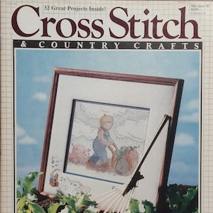 May include: A magazine cover for "Cross Stitch & Country Crafts", showing a framed cross-stitch picture of a child with a wheelbarrow and pigs. The magazine has text that reads "32 Great Projects Inside!" and "May/June 90".