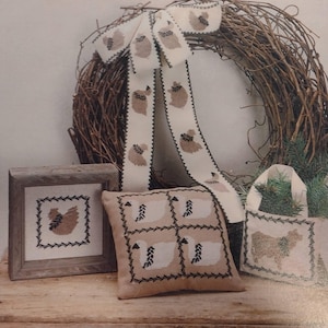 May include: A set of four cross-stitch projects featuring a brown rooster, a white chicken, and a brown cow. The projects are displayed on a wooden surface with a wreath in the background.