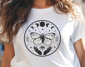以下が含まれることがあります： 白のTシャツ。前面に、蝶、月の満ち欠け、星、手、目などの黒と白の円形デザインがプリントされています。