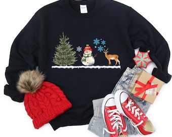May include: A black sweatshirt with a winter scene featuring a snowman, a deer, and a pine tree. The sweatshirt is paired with red knit beanie, blue jeans, and red converse shoes.