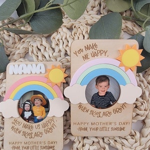 May include: Two wooden photo frames with rainbow and sun designs. The frames have a space for a photo and a message that says "You make us happy when skies are grey!" and "You make me happy when skies are grey!" The frames are decorated with a rainbow, clouds, and a sun. The frames are perfect for a Mother's Day gift.