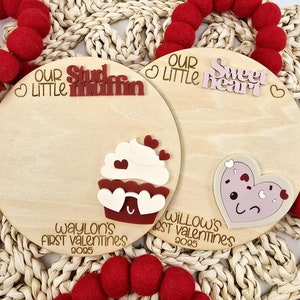 May include: Two wooden Valentine's Day signs with the text "Our Little Stud Muffin" and "Our Little Sweetheart" with a cupcake and a heart design. The signs also include the text "Waylon's First Valentine's 2025" and "Willow's First Valentine's 2025".