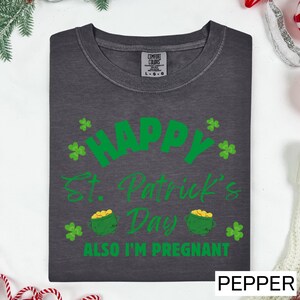 A gray t-shirt with a green design that says "Happy St. Patrick's Day" and "Also I'm pregnant" printed on it.