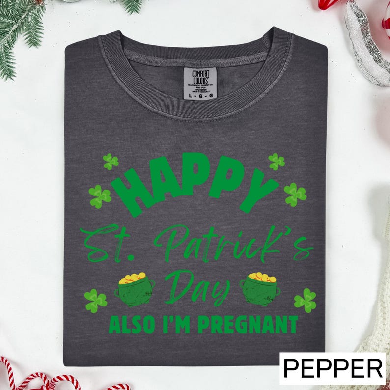 A gray t-shirt with a green design that says "Happy St. Patrick's Day" and "Also I'm pregnant" printed on it.