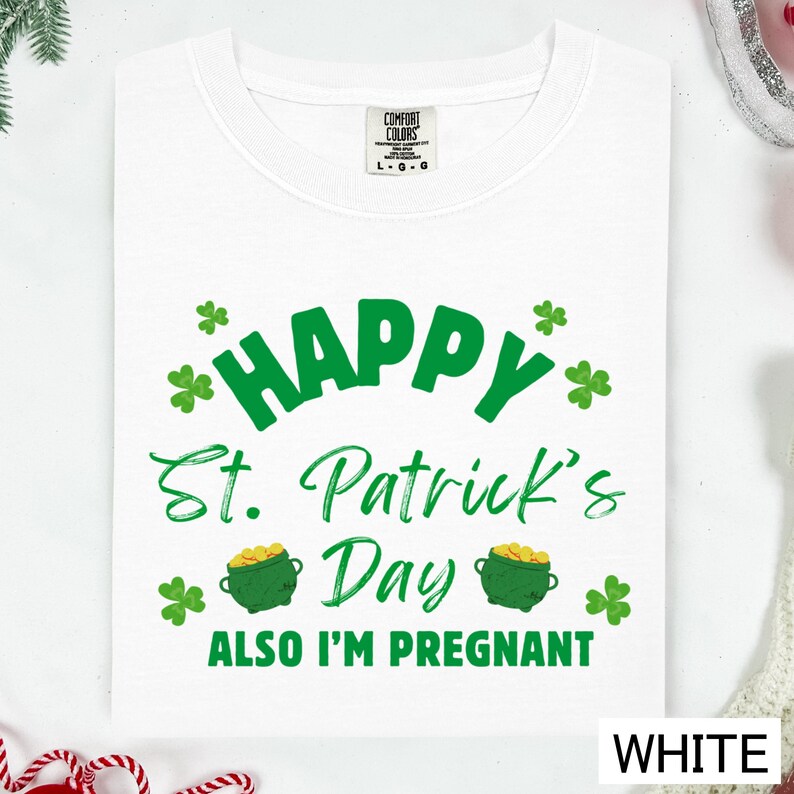 A white t-shirt with a graphic design that says "Happy St. Patrick's Day Also I'm pregnant" in green text.