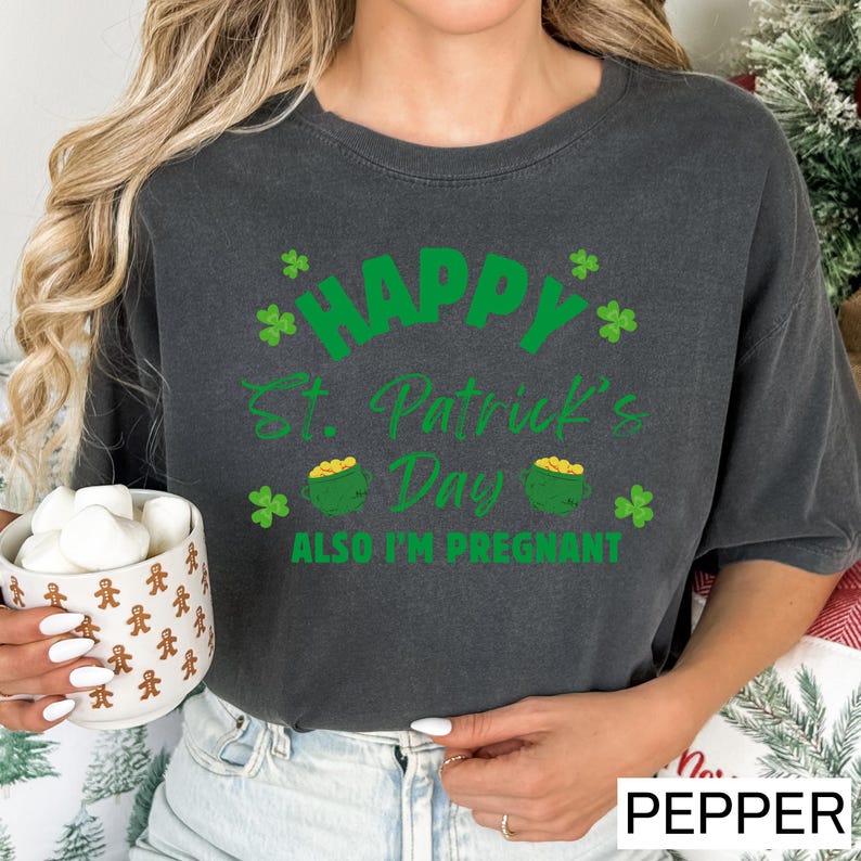 A woman wearing a gray t-shirt with a green design and text, holding a mug with marshmallows.