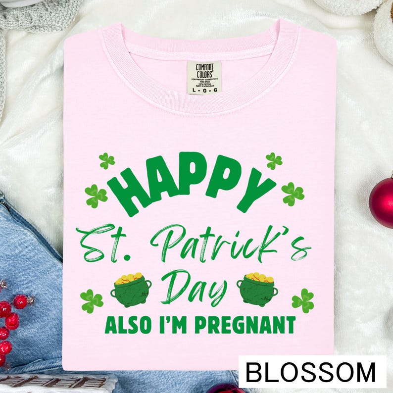 A pink t-shirt with a humorous text and graphics related to St. Patrick's Day, including the phrase "Happy St. Patrick's Day Also I'm pregnant" and a pot of gold coins.