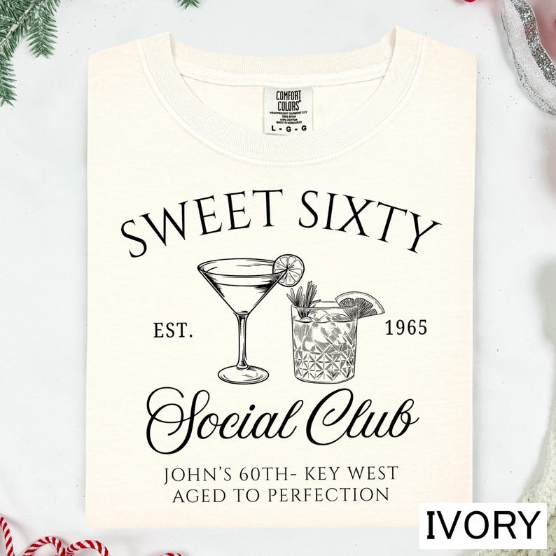 a white t-shirt with a graphic design that includes a cocktail glass and a text that reads "Sweet Sixty Social Club John's 60th - Key West Aged to Perfection".