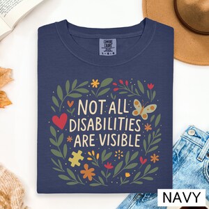 a blue t-shirt with a colorful graphic design and text, along with some other items such as a hat, a book, and a cup.