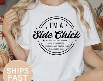 May include: White t-shirt with the text "I'M A Side Chick" in a black circular design. The design includes a list of side dishes. The shirt also has the text "WHITE" in a white rectangle.