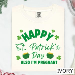 A white t-shirt with a green and white design that says "Happy St. Patrick's Day" and "Also I'm pregnant".