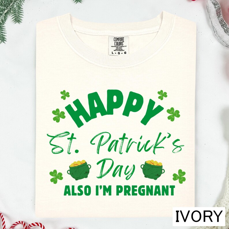 A white t-shirt with a green and white design that says "Happy St. Patrick's Day" and "Also I'm pregnant".