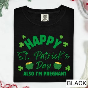 A black t-shirt with a green and white design that says "Happy St. Patrick's Day Also I'm pregnant" printed on it.