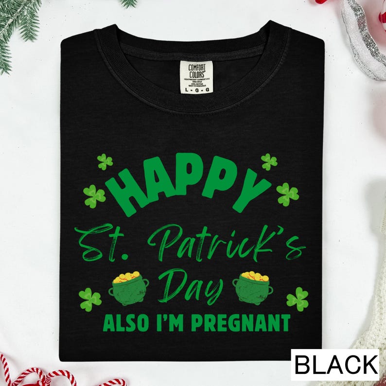 A black t-shirt with a green and white design that says "Happy St. Patrick's Day Also I'm pregnant" printed on it.