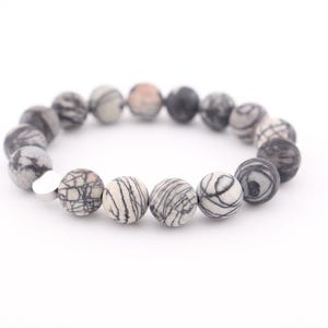 Peut inclure: Un bracelet composé de perles à motifs noirs et blancs. Les perles sont rondes et ont une finition lisse.