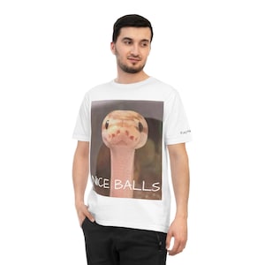 Könnte beinhalten: Weißes T-Shirt mit einem Schlangenbild und dem Text "NICE BALLS". Die Schlange hat ein hellbraunes und beiges Muster. Das T-Shirt hat einen Rundhalsausschnitt und kurze Ärmel. Das Wort "Reptile" ist auf dem Ärmel aufgedruckt.