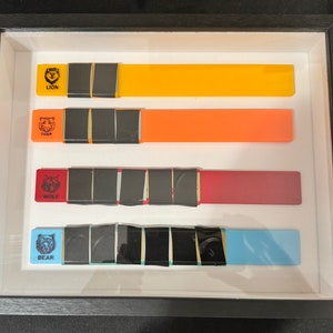 May include: Four framed rectangular plaques with different colored backgrounds and animal names. The plaques are arranged vertically, with the top plaque being yellow, the second orange, the third red, and the bottom blue. Each plaque has a black and white image of an animal and the animal's name printed in black below the image. The animal names are "Lion", "Tiger", "Wolf", and "Bear".