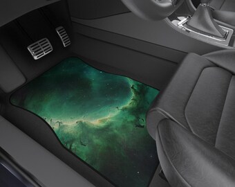 May include: Car floor mat with a vibrant green and teal nebula design. The mat is rectangular with a black border and is placed in the driver's side footwell of a car. The pedals and a portion of the car seat are visible.