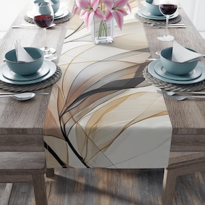 Puede incluir: Una mesa de comedor con un camino de mesa con estampado floral en tonos beige, marrón y negro. La mesa está puesta con cuencos, platos y copas de vino de color turquesa. Un jarrón con lirios rosas está en el centro.
