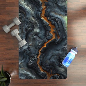 Puede incluir: Una esterilla de yoga con un diseño oscuro y abstracto con tonos grises, negros y naranjas, que se asemeja a tierra agrietada. Dos pesas grises y una botella de agua azul están colocadas sobre una superficie de madera.