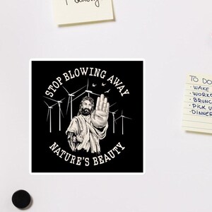 Op de afbeelding: Een zwart-witte sticker met een afbeelding van een man die zijn hand opsteekt voor een veld met windturbines. De tekst "Stop blowing away nature's beauty" staat in een cirkel rond de afbeelding.