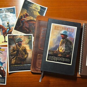 May include: A collection of historical military-themed prints and two notebooks. The prints feature illustrations of soldiers and pilots with text including "Buffalo Soldier," "Hellfighters," and "Keep 'Em Flying." A black notebook and a brown spiral notebook are included.