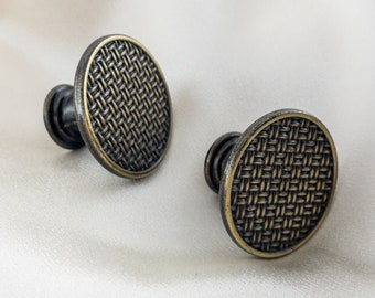 May include: Two antique gold-toned cabinet knobs with a woven pattern. The knobs have a round shape and a raised design.