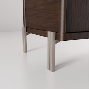 May include: A dark brown wooden cabinet with a curved edge and silver-colored metal legs. The legs are rectangular and have a vertical groove down the center. The cabinet is set against a white background.
