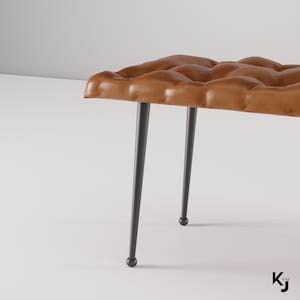 May include: A brown leather bench with a tufted design and black metal legs. The bench has a modern and minimalist style.
