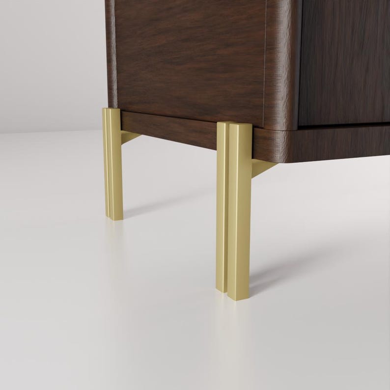 May include: A close-up of a dark brown wooden cabinet with gold-colored metal legs. The cabinet has a curved edge and a smooth finish. The legs are rectangular and provide support.