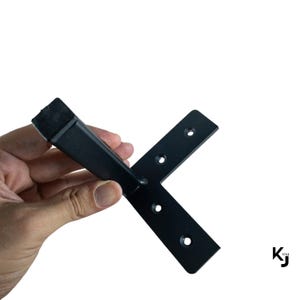 May include: Black metal L-shaped bracket with multiple holes for mounting. The bracket has a straight leg and a shorter leg that is perpendicular to the straight leg.