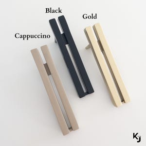 May include: Three cabinet pulls in black, gold, and cappuccino colors. Each pull has a rectangular design with a vertical bar and a horizontal bar. The word "Black", "Gold", and "Cappuccino" are written above each pull.