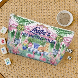An overhead view of a personalized chinoiserie-design Mahjong tile storage bag surrounded by dice, Mahjong tiles, and coins on a woven rattan tabletop.