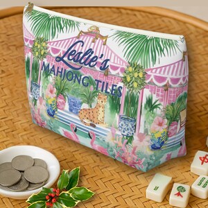 A Mahjong tile tote bag on a rattan surface beside Mahjong tiles, coins, and a sprig of holly. The design features pink, green, and blue tropical Chinoiserie design.