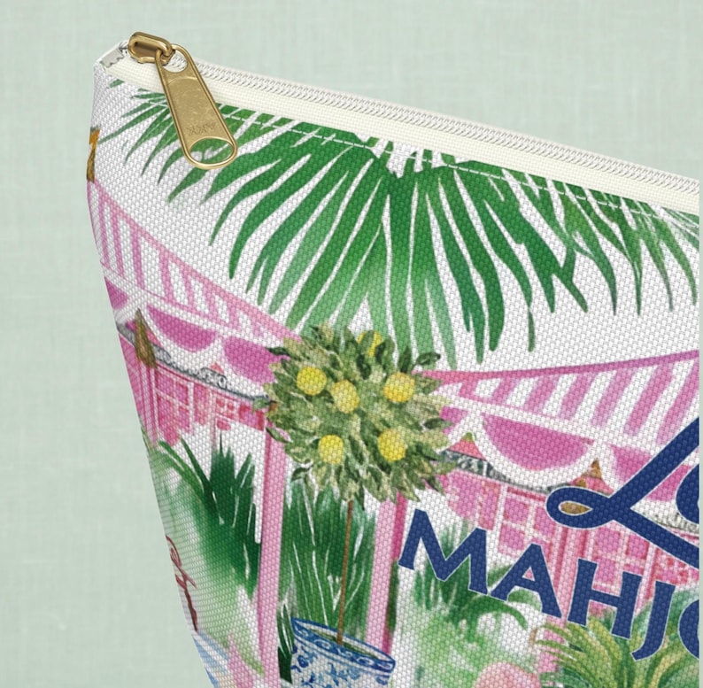 A close-up of a personalizable mahjong zippered tile storage bag highlighting the bag’s fabric texture and gold zipper. The print shows palm leaves and pink stripes on woven canvas.