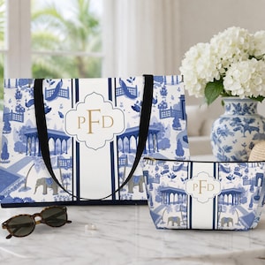 May include: A tote bag and a cosmetic bag with a blue and white toile pattern featuring elephants, pavilions, and peacocks. Both bags have a white center stripe with the initials "PFD" in gold. The tote bag has black handles.