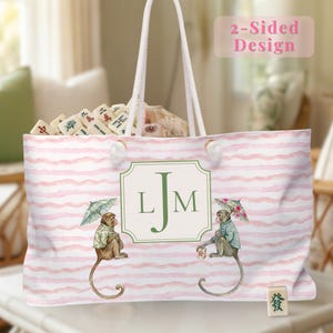 May include: A large tote bag with a pink and white striped pattern. The bag features a watercolor design of two monkeys holding umbrellas. The bag has a white rope handle and a monogram with the letters "LJM". The bag is filled with Mahjong tiles.