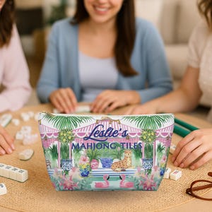 Three women sit around a table playing Mahjong. A colorful personalized Mahjong tile bag sits upright in the center of the table. Tile bag features a custom name and a preppy chinoiserie print with striped cabana, cheetah and potted lemon trees.