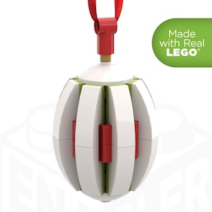 May include: A white and red ornament made with LEGO bricks. The spherical ornament has white panels with red and green accents. A red ribbon is attached to the top. The text "Made with Real LEGO" is on the right side.