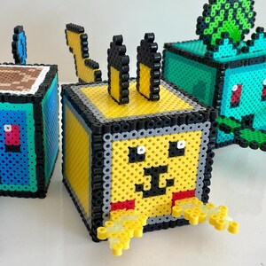 May include: Four colorful pixelated cube-shaped figures, each with a different Pokemon character. The characters are Charmander, Squirtle, Pikachu, and Bulbasaur.