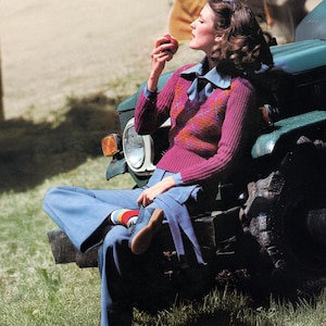 Puede incluir: Una mujer con un suéter morado con un patrón colorido, una camisa azul y pantalones azules. Está sentada en un vehículo verde y comiendo una manzana. El atuendo es reminiscente de la moda de los años 70.