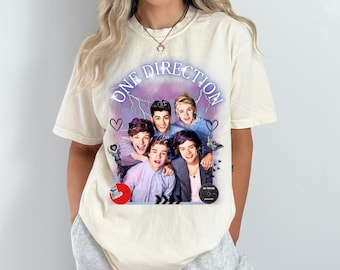 Peut inclure: T-shirt ivoire avec un graphisme du groupe One Direction. Le graphisme comprend le nom du groupe et des images des membres du groupe. Le t-shirt est de style col rond et à manches courtes.