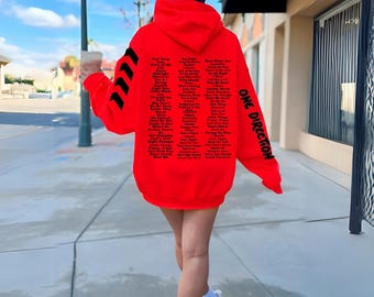 Può includere: Felpa rossa con una stampa nera delle parole "One Direction" e un elenco dei loro titoli di canzoni.